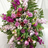 Tall cascading arrangement of purple roses, pink lilies, and white filler flowers in an oval spray shape.