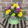 Colorful mixed flower arrangement in a green pot with a butterfly pick