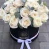 White roses arranged in a black round box with a lavender ribbon