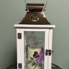 A white wooden lantern with a soft purple lilac spray and butterfly