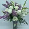 White roses and purple lilacs arranged in a clear glass vase