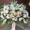 All-white lilies and roses form the commanding centerpiece of this sympathy flower