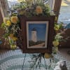 A framed lighthouse painting rests at the heart of this sympathy wreath