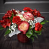 The centerpiece style bouquet is designed in a red glass container with