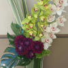 Orchid and purple chrysanthemum arrangement in a tall glass vase