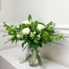 White and green floral arrangement in a glass vase with a ribbon