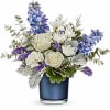 White roses and mums with blue delphinium and purple accents in a blue glass vase