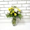 Small bouquet of yellow and white daisies arranged with greenery in a clear glass vase