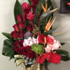 Tall tropical bouquet with red roses, anthuriums, and orchids in a gold vase