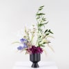 Tall floral arrangement in a black vase with purple, white, and blue blooms