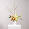 Peach roses and white-green flowers in a white vase with bare branches