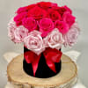 Pink and red roses arranged in a black hat box with a red ribbon