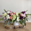 Low floral centerpiece in a white vase with pink, white, and purple blooms
