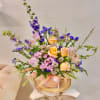 Pastel roses and purple flowers arranged in a pink hat box
