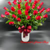 Tall white vase filled with many red roses and foliage, finished with a large red satin bow