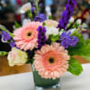 Pink gerbera daisies and purple flowers in a glass vase