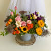 Mixed bouquet with roses, tulips, sunflowers, and purple blooms in a gray container