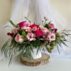 Pink rose bouquet in a white vase with trailing greenery