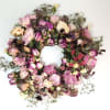 Dried floral wreath with pink and purple blooms on a white background