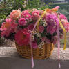 Pink and peach flowers arranged in a wicker basket with ribbon.