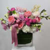 Pink and white floral arrangement in a clear square vase with a satin ribbon