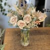 Blush roses arranged in a clear glass vase with dried grasses and filler flowers.
