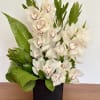 Arrangement of white orchids with burgundy centers and large green leaves in a black cube vase