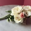Flowers: The corsage is primarily composed of spray roses in cream and