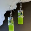 A pair of lime-green rectangular glass dangle earrings that catch the light