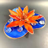 A vivid orange stained-glass water lily crowns a marbled blue base in