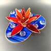 A bold red and orange stained-glass water lily mounted on a marbled