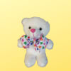 White teddy bear with a colorful heart-pattern bow on a yellow background
