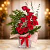 Arrangement of red roses with white filler flowers in a square glass vase wrapped with a red bow