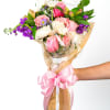 Handheld bouquet of pink, white, and purple mixed flowers wrapped in cellophane with a large pink bow