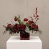 Red floral arrangement in a square glass vase with berries and greenery