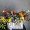 Colorful floral arrangement in a white pleated container with blue and yellow blooms
