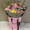 Mixed bouquet of pink roses, yellow blooms, and lavender flowers in a pink gift bag