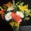 Bright citrus tones of orange roses and yellow lilies make this flower