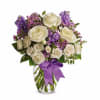 White roses and purple flowers arranged in a clear glass vase with a purple ribbon bow