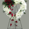 Heart-shaped floral wreath with red roses and white flowers on a stand