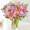 Pink lilies, roses, and lavender flowers in a clear glass vase