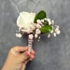 White rose boutonni&egrave;re with pale pink baby's breath and glossy green leaves