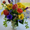 Colorful mixed bouquet in a clear glass vase with tulips, daisies, and ranunculus