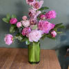 Pink peonies and orchids arranged in a green glass vase