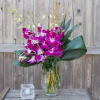 Purple orchid arrangement in a clear glass vase with broad leaves