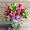 Mixed bouquet of pink, purple, and red flowers in a clear glass vase