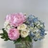 Pink peonies, white roses, and blue hydrangeas in a square glass vase
