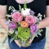 Handheld bouquet of pink, white, purple, and peach flowers in a glass vase