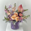Peach roses and purple flowers in a purple vase with silver foliage