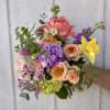 Handheld bouquet of pink, peach, purple, and yellow flowers